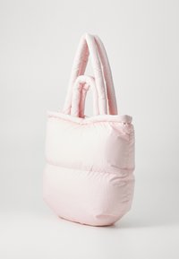 Sac fourre-tout rose en peluche avec une texture douce matelassée et deux poignées en forme de boucle. Forme carrée avec un large dessus ouvert. Design minimaliste.