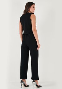 Black jumpsuit with sleeveless design, tapered legs, and a cropped top. Paired with high-heeled shoes featuring a snake print accent.
