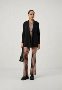 Svart blazer over en taupe topp, kombinert med brune, tie-dye flared bukser med bølgede kanter. Svart veske og kraftige svarte sko fullfører utseendet.