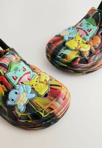 Des Crocs noirs et colorés avec des charms de personnages Pokémon en relief. Le matériau est flexible, avec des trous de ventilation et un design sportif.