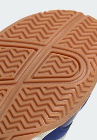 Semelle de chaussure en caoutchouc présentant un motif en zigzag orange avec des rainures pour une meilleure adhérence, bordée d'un matériau supérieur bleu et blanc.