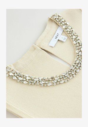 Kremowy sweter z okrągłym dekoltem, ozdobiony koralikowym kołnierzem z przezroczystych cyrkonii i teksturowanej tkaniny. Widoczna metka rozmiaru.