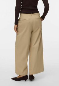 Bēša krāsas plaša stila bikses no gludas auduma, ar aizmugurējām kabatām un ērtu piegriezumu. Kopā ar tumšiem koniskiem papēžiem.