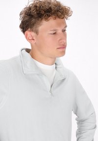 Hellgrauer Fleece-Pullover mit Reißverschlusskragen, weicher Textur und langen Ärmeln, ausgestattet mit einem subtilen Stichdetail entlang der Nähte.