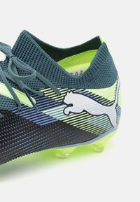 Scarpe da calcio blu scuro e verde lime con tomaia testurizzata, colletto in rete e tacchetti moldati, caratterizzate da un logo Puma bianco e un design a strisce.