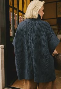 Navy-blauer Strickponcho mit Wellenmustern und hohem Kragen. Verfügt über weite Ärmel und eine lockere Passform, strukturierter Stoff und gerippter Saum.