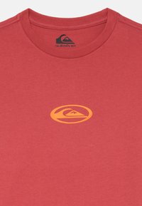 Rød bomull t-skjorte med rund hals. Sentrert, oransje Quiksilver-logo trykket på brystet. Glatt tekstur med en avslappet passform.