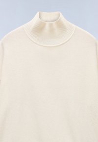 Turtleneck sweater i cremefarve med ribstrikket krave og glat tekstureret stof på kroppen og ærmerne.