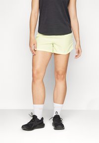Light green running shorts made of lightweight fabric, paired with a black top, white socks, and black athletic shoes, showcasing a casual athletic style.