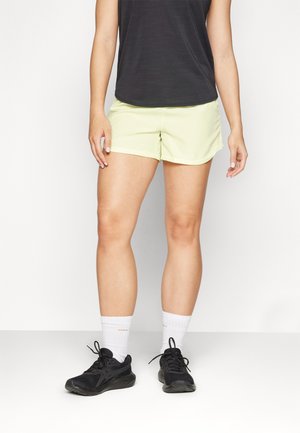 Lys grønn løsshorts laget av lett materiale, kombinert med en svart topp, hvite sokker og svarte treningssko, som viser en avslappet atletisk stil.