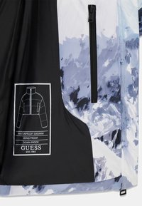 Zwart-wit jack met een blauw en grijs abstract patroon, waterdicht, winddicht, met een rits aan de voorkant en een merklabel.