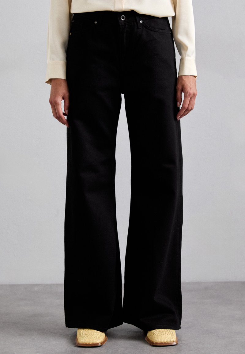 Black wide-leg pants made of denim, featuring a high waist, subtle stitching details, and a smooth texture. Paired with yellow woven shoes.