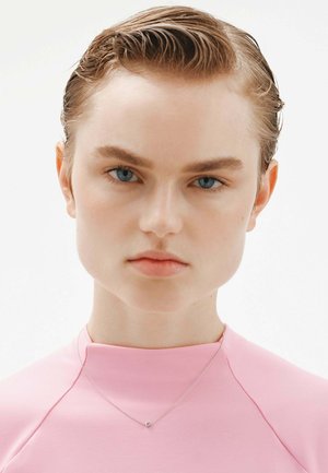 Top rosa ajustado con un cuello alto, que presenta un collar plateado con un pequeño colgante. Tejido suave y diseño minimalista.