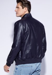 Chaqueta bomber de cuero azul marino con ribetes en el dobladillo y los puños, textura suave y cuello alzado, combinada con jeans de color azul claro.