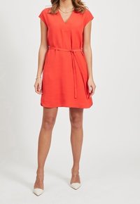 Czerwona sukienka z krótkim rękawem, dekoltem w kształcie V i paskiem w talii. Wykonana z gładkiego materiału, ma luźny krój i sięga ponad kolana.