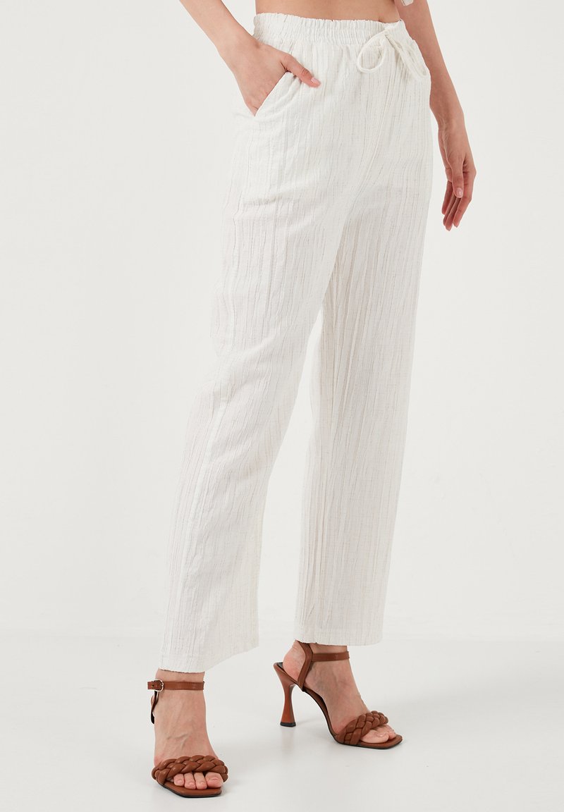 Pantalones anchos de color blanco, texturizados, con cintura elástica y cordón. Con bolsillos laterales. Combinados con sandalias de tacón marrones.