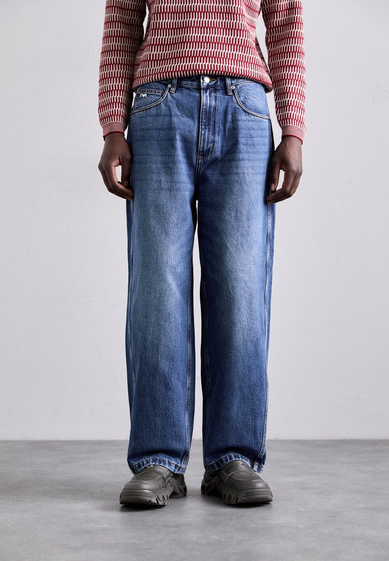 Blauwe denim jeans met een relaxed fit, voorzien van een klassiek vijf-pocket ontwerp en contrasterende stiksels. Gecombineerd met grijze schoeisel.