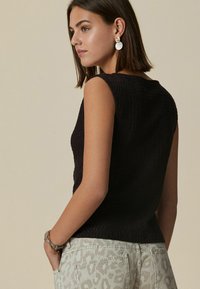 Haut sans manches noir texturé, avec un col rond et une coupe ajustée, associé à un pantalon gris clair à imprimé léopard et des boucles d'oreilles dorées.