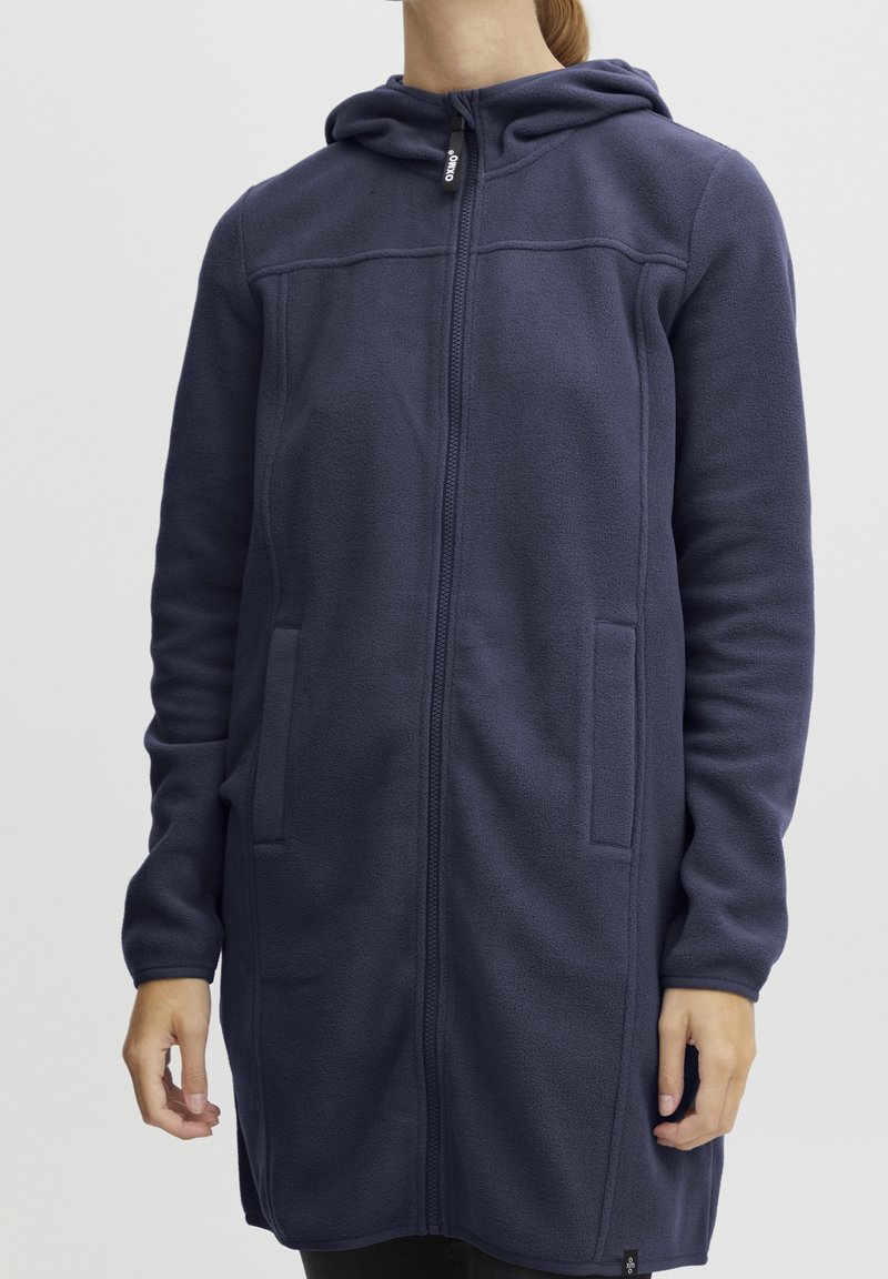 Sudadera con cremallera completa en color azul marino, con bolsillos laterales y un diseño largo y casual. Tejido texturizado, acabado suave y capucha ajustable con cordón.