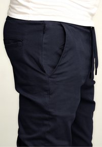 Navy Jogginghosen aus weichem Stoff mit glatter Textur. Merkmale sind ein elastischer Bund, ein Kordelzug und eine seitliche Reißverschlusstasche.
