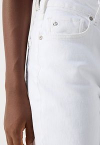 Jeans de mezclilla blanca con corte ajustado. Presentan bolsillos laterales y traseros, herrajes plateados y una textura sutil.