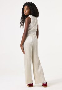 Zilveren geribbelde twee-delige set met een mouwloos top en wijde broek. De outfit heeft een soepele textuur en is gecombineerd met schoenen met rode zolen.