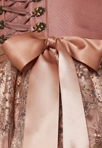 Robe rose avec un corsage texturé orné de boutons décoratifs, un nœud en ruban satin et une jupe en dentelle embellie de perles et de motifs complexes.