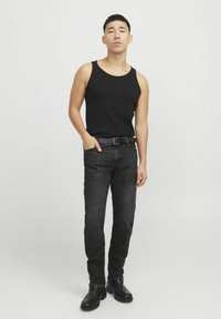 Crni rebrasti top, tamne traperice i crne čizme do gležnja. Outfit se ističe prilagođenim dizajnom s klasičnom siluetom i minimalnim detaljima.