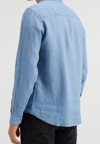 Ljusblå linne skjorta med lång ärm, rundad nederkant, knäppta manschetter och en design med rygghöft. Slät textur och avslappnad passform.