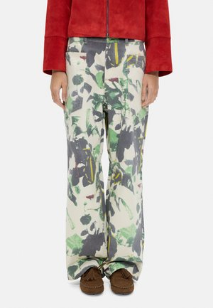 Spodnie o szerokich nogawkach z zielonym, szarym i żółtym abstrakcyjnym nadrukiem roślinnym, zestawione z brązowymi mokasynami i czerwonym, krótkim żakietem.