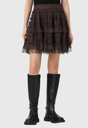 Czarna warstwowa mini spódnica z koronki w połączeniu z wysokimi czarnymi skórzanymi kozakami, na stojącej osobie na jednolitym tle.