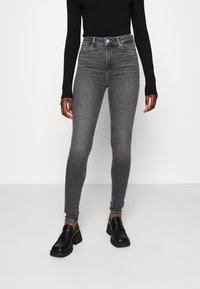 Jeans ajustados de cintura alta en denim gris deslavado, con un diseño clásico de cinco bolsillos y detalles de costura sutiles, combinados con mocasines negros.