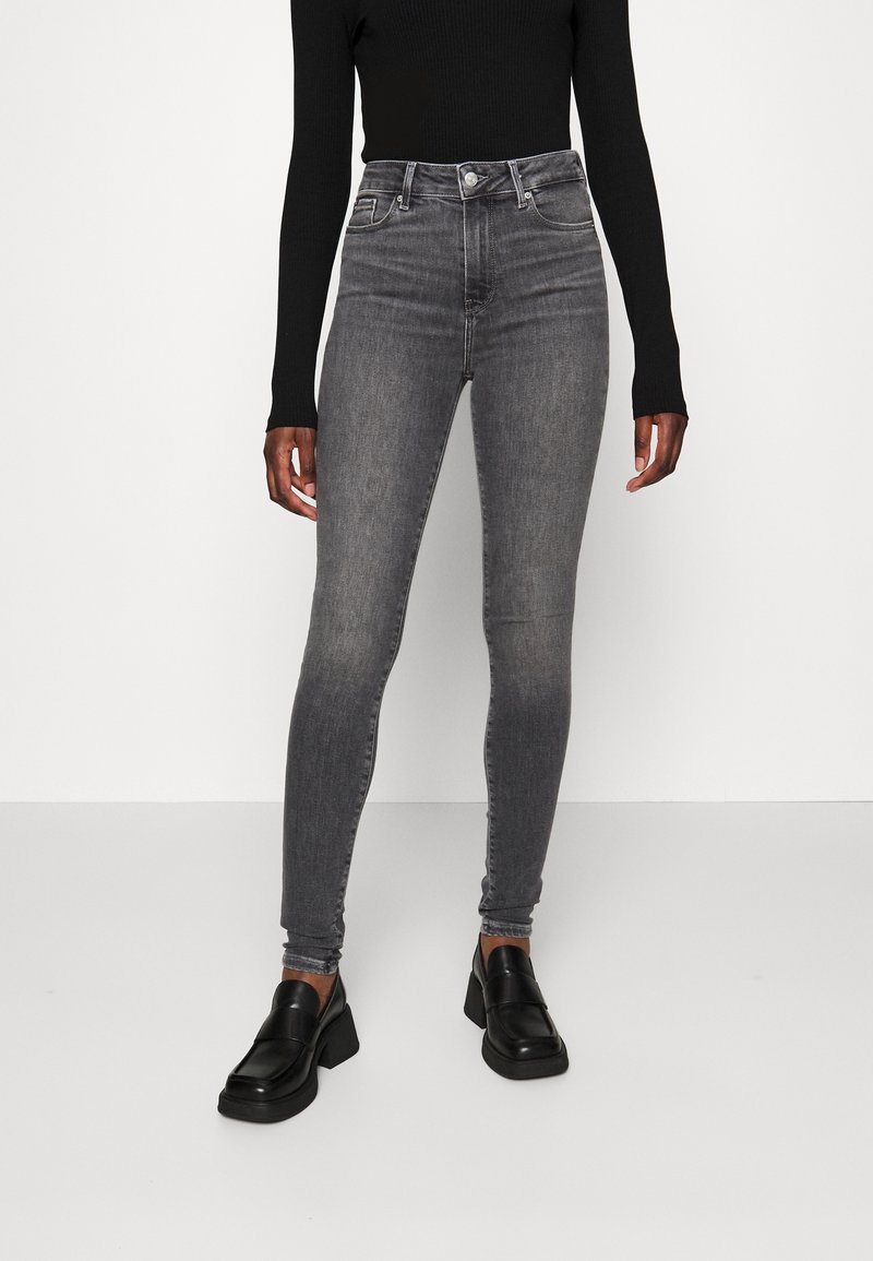 Jeans ajustados de cintura alta en denim gris deslavado, con un diseño clásico de cinco bolsillos y detalles de costura sutiles, combinados con mocasines negros.