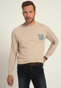 T-shirt beige a maniche lunghe con scollatura rotonda, con testo e numeri blu nella parte sinistra del petto. Tessuto di cotone liscio, vestibilità comoda.