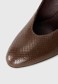 Bruine, glanzende nepleren schoen met een getextureerd slangenhuidmotief, puntige neus en een open uitsnijding aan één zijde voor een strak ontwerp.