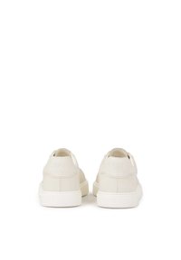 Zapatillas blancas de cuero con una textura suave, diseño minimalista y logotipo grabado en el talón. Cuentan con una gruesa suela de goma blanca.
