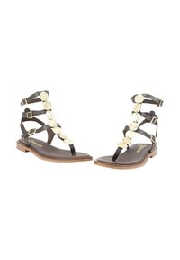 Sandalias negras de tiras con acentos de círculos metálicos, suela plana y hebillas. Fabricadas con un material similar al cuero y con una textura suave.