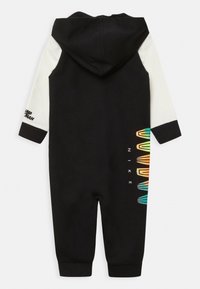 Černý overal s kapucí a bílými rukávy, na kterém jsou multikolorové geometrické vzory a nápis "NIKE" po straně. Měkký materiál, manžetové kotníky.