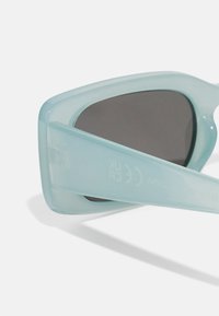 Des lunettes de soleil couleur aqua avec une monture rectangulaire élégante, des verres foncés et une texture lisse et brillante. Présentent un logo sur la branche latérale.