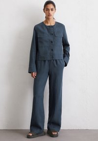 Donkerblauwe, lichte linnenoutfit bestaande uit een cropped jasje met vier zakken en bijpassende wijdvallende broek, gecombineerd met gestructureerde zwarte schoenen.