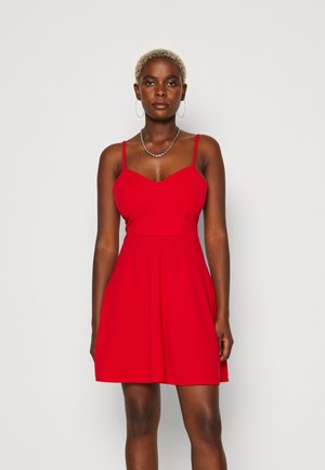 Red sleeveless dress with a fitted bodice, V-shaped neckline, and flared skirt. Made from smooth fabric, featuring thin straps and a waist seam.