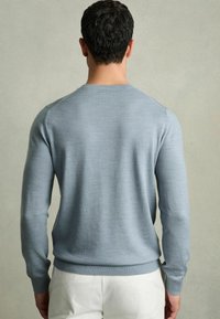 Világoskék, hosszú ujjú pulóver, kerek nyakkivágással, bordázott mandzsettákkal és aljjal. Az anyag lágy és kötöttnek tűnik.