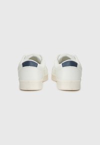 White sneakers with a smooth leather finish, textured heel tab in navy, and tan rubber sole. Features a low-profile design and rounded toe.
