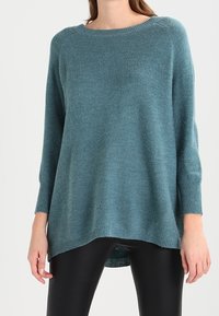 Miętowy dziany sweter z okrągłym dekoltem, długimi rękawami i luźnym krojem. Posiada ściągacze na mankietach oraz lekko wydłużony tył.