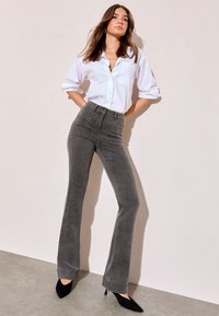 Harmaat levenevät farkut, joissa on etutaskut, yhdistettynä valkoiseen napitettuun paitaan. Malli käyttää mustia terävät kärjet omaavia korkokenkiä. Sileä pintamateriaali, rento muotoilu.