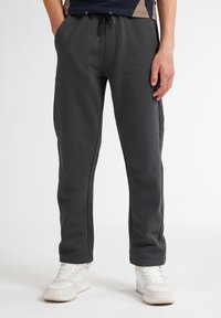 Mörkgrå sweatpants i mjukt material, med dragsko i midjan, smalnande ben och diskreta sidofickor. Bärs med vita sneakers.