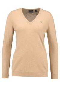 Maglione lavorato a maglia beige con maniche lunghe, design a scollo a V, polsini e orlo ribattuti, caratterizzato da un piccolo logo sul lato sinistro del petto. Texture morbida.