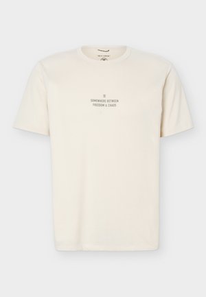 Cream-colored short-sleeve t-shirt with round neck and centered text reading "Somewhere between freedom & chaos" in small gray font.