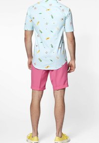 Camicia a maniche corte di colore azzurro chiaro con motivi colorati, abbinata a pantaloni corti rosa e scarpe gialle. Tessuto liscio con una vestibilità casual.