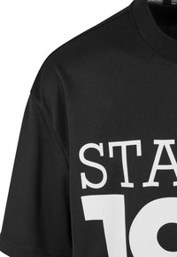 Crni sportski dres napravljen od prozračnog mrežastog materijala. Ima veliki bijeli natpis "STATE 19" otisnut sprijeda. Kratki rukavi i okrugli izrez.